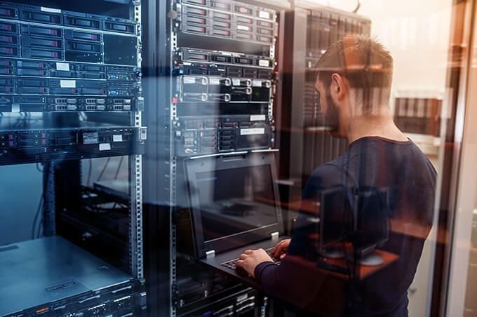 IT technician working on a laptop in front of server racks in a data center