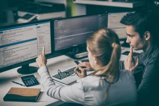 Two developers reviewing code on multiple screens